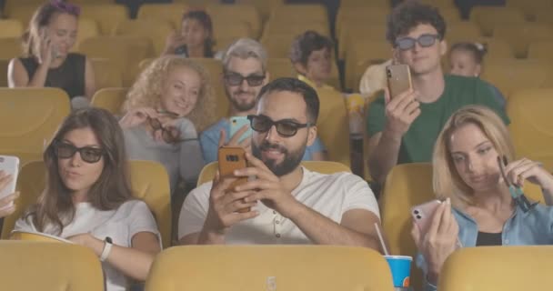 Groupe de film-aime utiliser des smartphones avant le film dans le cinéma 3D. Portrait d'hommes et de femmes multiethniques détendus prenant des selfies et surfant sur Internet avant leur première au cinéma. Siège social Cinema 4k ProRes. — Video