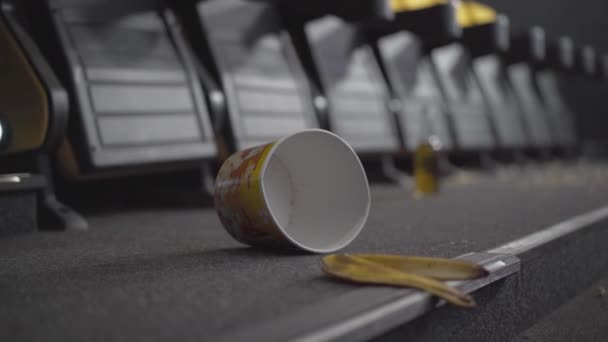 Close-up van lege popcorn doos en bananenschil liggend op de vloer in de bioscoop. Vuil achtergelaten door bezoekers in de bioscoop. — Stockvideo