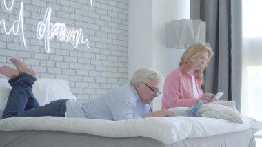 Kıdemli eş kocalarına dokunuyor ve rahatsız ortağın eşini görmezden gelirken gülümsüyor. İnternet işi için kablosuz mesaj kullanan orta yaşlı bir adamın geniş açılı portresi. Stresli uzaktan kumanda çalışıyor.