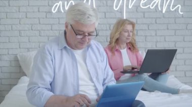 Laptop klavyesinde daktilo yazan yakışıklı, kameraya bakıp gülümseyen. Arka planda internette sörf yapan bulanık bir kadın. Covid-19 'da online çalışan mutlu orta yaşlı beyaz adam portresi..