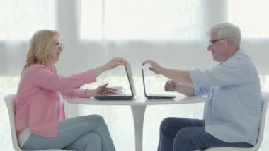 Uzaktan çalışmadan sonra tatmin olmuş yaşlı çift beşlik çakıyor. Mutlu orta yaşlı adam ve kadın dizüstü bilgisayarları kapatıp gülümsüyor. Covid-19 karantinasında çalışan olgun, beyaz bir ailenin yan görünüşü.