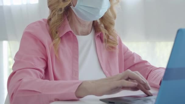 Mulher idosa irreconhecível na máscara facial digitando no teclado do laptop. Empresária caucasiana a trabalhar em casa na quarentena pandémica de Covid-19. Estilo de vida empresarial do Coronavirus. — Vídeo de Stock