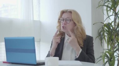 Kendinden emin beyaz bir öğretmenin portresi. Dizüstü bilgisayarın önünde konuşan son sınıf öğrencisi ciddi bir kadın. Gözlüklü kadın öğretmen Covid-19 salgınıyla ilgili online ders veriyor..