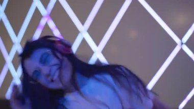 Güneş gözlüklü, kulaklıklı, neon ışıklarda dans eden neşeli bayan DJ. Gece kulübünde eğlenen pozitif beyaz kadın portresi. Gülümseyen güzel bayan eğleniyor..