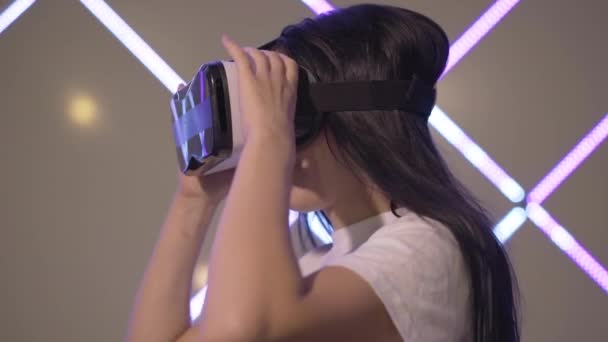 Vista lateral de mujer joven sorprendida en gafas 3D mirando las manos en realidad virtual. Emocionado jugador femenino caucásico descansando en el club VR. Milenial mujer jugando juegos en línea utilizando tecnologías modernas — Vídeos de Stock