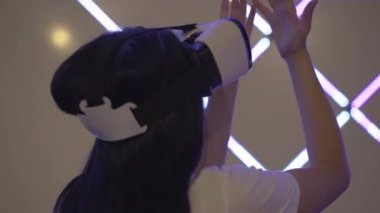 VR gözlüklü neşeli, heyecanlı kadının neon ışıklarda ve hareketli ellerde duruşu. Beyaz kadın oyuncu sanal gerçekliğin tadını VR kulübünde çıkarıyor. Modern artırılmış gerçeklik oyunu.