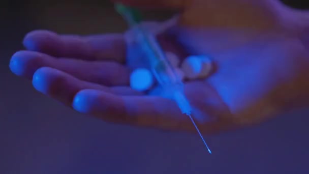 Großaufnahme einer männlichen kaukasischen Hand mit Tabletten und Spritze im Neonlicht. Unbekannter Drogendealer hält Drogen in Nachtclub Mann mit illegalem Opioidhandel von Polizei bei Blaulicht und Rotlicht erwischt. — Stockvideo