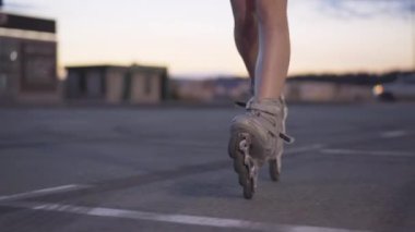 Boş otoparkta alacakaranlıkta paten giyen zayıf kadın bacakları. Kentte akşam vakti paten kayan tanınmamış genç beyaz kadın. Hobi ve boş zaman kavramı.
