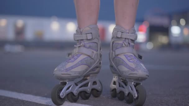 La cámara va desde los pies femeninos en rodillos a la cara sonriente de la hermosa mujer joven mirando a la cámara. Retrato de patinador positivo parado al atardecer en la ciudad. Mujer feliz patinando por la noche. — Vídeo de stock