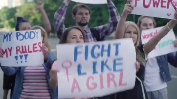Een menigte activisten met spandoeken voor feminisme schreeuwend op straat. Portret van mannelijke en vrouwelijke demonstranten die vechten voor vrouwenrechten. Groep Kaukasische mensen die vechten voor gendergelijkheid. — Stockvideo