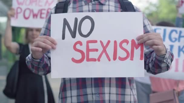 Homme méconnaissable tenant pas de pancarte de sexisme comme groupe de personnes protestant en arrière-plan. Manifestation anti-discrimination des militants caucasiens. Émeute féministe sur la défense des droits des femmes. — Video