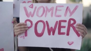 Kameralar aktivistlerin elinde feminist pankartlar boyunca hareket ediyor. Pankartlarda kadın hakları sloganlarının yakın plan çekimleri. Cinsiyet eşitsizliğini protesto eden tanınmamış insanlar. Feminizm kavramı.