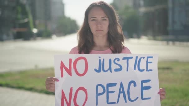 Joven mujer caucásica protestando contra la discriminación y los prejuicios. Retrato de un hermoso demostrador serio con pancarta de pie a la luz del sol. Activista luchando por la democracia. — Vídeos de Stock