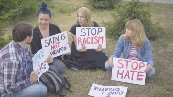 Sitzprotest der kaukasischen Bevölkerung gegen Menschenrechtsverletzungen. Männliche und weibliche Aktivisten mit Anti-Rassismus-Transparenten sitzen auf Gras und reden. Demonstranten kämpfen für Gleichstellung der Geschlechter. — Stockvideo