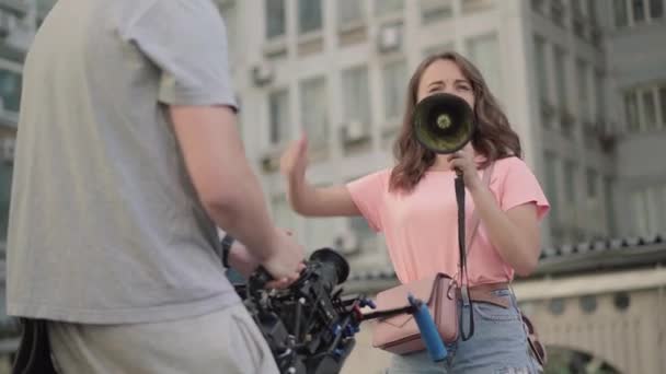 Caméraman méconnaissable tirant jeune belle femme avec mégaphone parler. Militante caucasienne en manifestation urbaine contre la discrimination des droits de l'homme ou la pollution environnementale. — Video