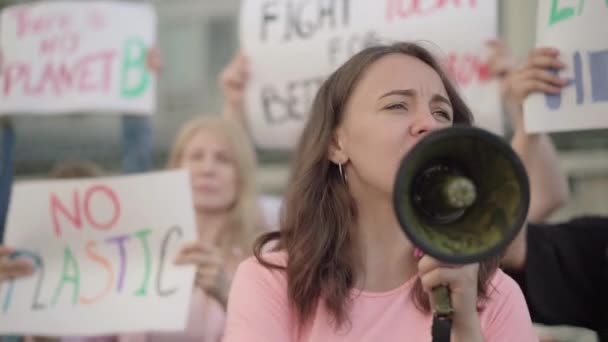 Joven mujer eco-activista gritando a través de megáfono con multitud de personas en el fondo. Grupo de hombres y mujeres caucásicos insatisfechos que protestan contra la contaminación ambiental. — Vídeo de stock