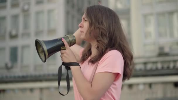 Young eco-activist shouting through megaphone and people with banners joining leader in demonstration. Portrait of worried Caucasian woman encouraging crowd to protest against environmental pollution. — Stock Video