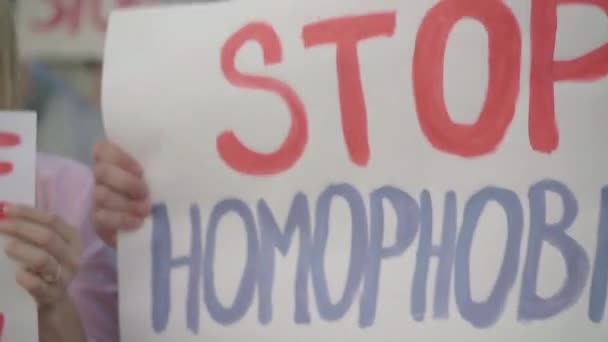 La cámara se mueve a lo largo de la fila de carteles anti-homofobia. Activistas caucásicos con pancartas gritando en manifestación sobre los prejuicios contra las personas homosexuales. Orgullo LGBT. — Vídeos de Stock