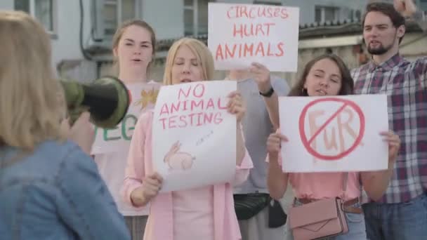 Multitud de personas que defienden los derechos de los animales en la ciudad urbana con una mujer borrosa gritando a través del megáfono al frente. Grupo de eco-activistas masculinos y femeninos en manifestación. — Vídeo de stock