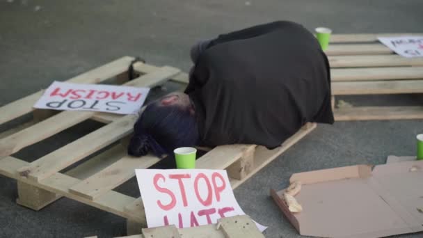 Young woman sleeping on pallet with anti-racist banners lying around. Female activist resting after demonstration for human rights. Concept of defending of ethnic equality.