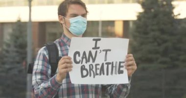 Yüzü maskeli yakışıklı bir adam. Dışarıda güneşli havada bayrak bile çekemiyorum. Sosyal eşitsizliğe karşı gösteri yapan genç beyaz protestocunun portresi. Sinema 4k ProRes Merkezi.