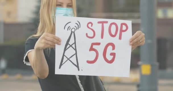 Mujer de confianza en la máscara de la cara estiramiento Stop 5G cartel. Retrato de un serio eco-activista caucásico protestando contra el impacto dañino de las torres móviles que causan la pandemia de Covid-19. Sede del cine 4k ProRes. — Vídeo de stock