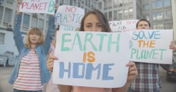 El retrato de una mujer sosteniendo la Tierra es un póster casero y mirando a la cámara. Manifestante de pie con pancarta mientras eco-activistas gritando en el fondo. Protección del medio ambiente. Sede del cine 4k ProRes. — Vídeo de stock