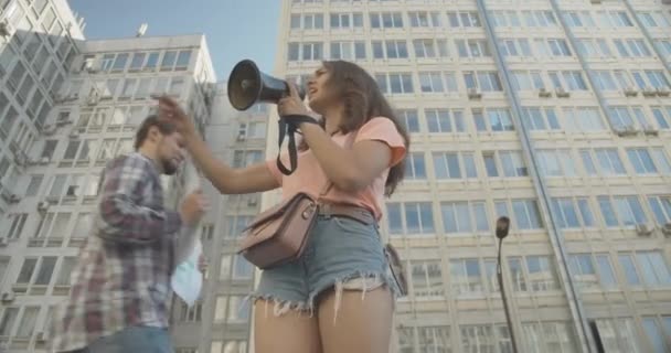 Vista del ángulo inferior de la joven activa gritando a través de megáfono como personas que vienen con pancartas de demostración en el fondo. Motín de eco-activismo contra la contaminación de la naturaleza. Sede del cine 4k ProRes. — Vídeo de stock