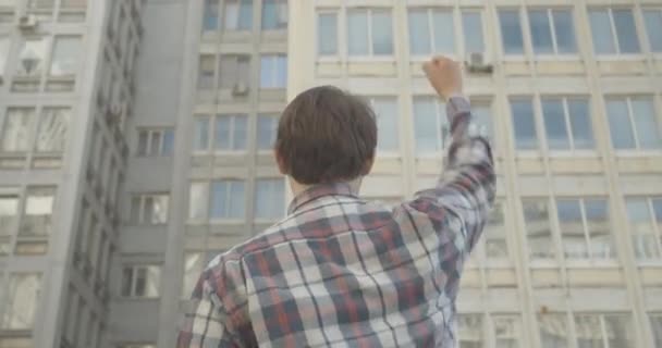 Vista trasera de morena hombre caucásico levantando el puño delante del edificio urbano. Activista irreconocible que protesta contra la desigualdad social o por los derechos humanos. Sede del cine 4k ProRes. — Vídeos de Stock