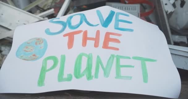 Κοντινό πλάνο του Σώστε τον πλανήτη πλακάτ που βρίσκεται στα σκουπίδια. Έννοια του οικολογικού ακτιβισμού και της περιβαλλοντικής ρύπανσης. Επιβλαβείς επιπτώσεις στο οικοσύστημα. Κινηματογράφος 4k ProRes HQ. — Αρχείο Βίντεο