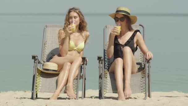 Portrait de deux femmes heureuses qui prennent des verres et boivent du jus en arrière-plan d'une mer ou d'un océan sans fin. Jeunes touristes caucasiens bronzés profitant de vacances sur la station estivale. — Video