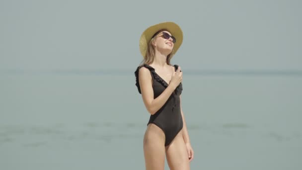 Belle femme confiante pulvérisant de la crème solaire sur un corps mince magnifique à la côte. Portrait de jeune touriste caucasien heureux appliquant crème solaire à la station estivale et souriant. — Video