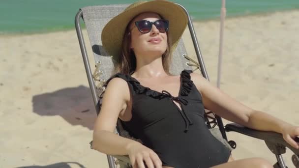 Fiduciosa donna sorridente che si gode la giornata di sole al resort estivo. Ritratto di giovane felice magro turista caucasico che prende il sole sul lettino sulla spiaggia sabbiosa all'aperto. — Video Stock