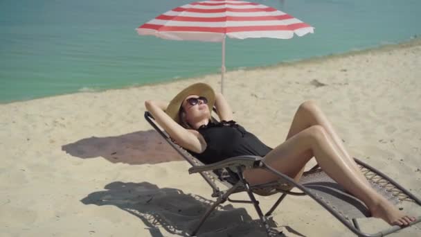 Plan large de belle femme détendue allongée sur une chaise longue et souriante. Portrait de heureux jeune touriste mince reposant sur la plage de sable fin à l'extérieur. Riches dame caucasienne profiter des vacances à la station estivale. — Video