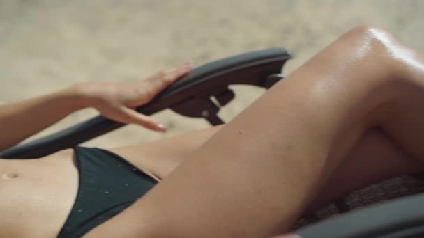 Kamera, güneşlenirken güneşlenen beyaz tenli güzel bir kadının muhteşem bronzlaşmış ince vücudu boyunca hareket ediyor. Güneşli yaz tatilinde kumsalda dinlenen bronzlaşmış turist portresi.. — Stok video