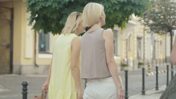 Vista trasera de tres mujeres emocionadas caminando por la calle de la ciudad y admirando los edificios. Mediados de adultos elegantes turistas caucásicos descansando en la ciudad extranjera en el soleado día de verano al aire libre. Turismo y ocio. — Vídeos de Stock