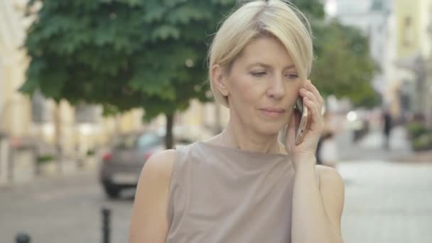 Elegante dama de mediana edad hablando por teléfono en la calle de la ciudad de verano. Retrato de una exitosa empresaria confiada colgando un teléfono inteligente y sonriendo a la cámara. — Vídeo de stock