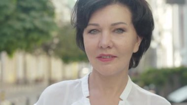 Şık, kendine güvenen, orta yaşlı bir kadının yaz günü şehir sokağında dikilip etrafa bakınması. Yurtdışına seyahat eden güzel esmer beyaz kadın portresi. Turizm konsepti.