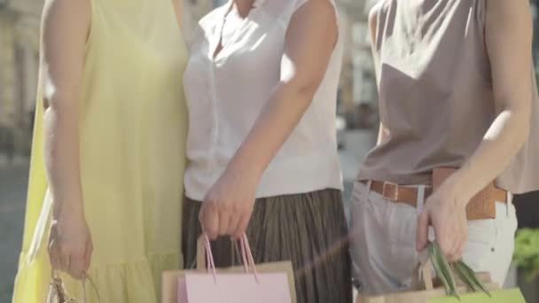 Tři nerozeznatelné bělošky natahují nákupní tašky na kameru. Dospělé ženy nakupující na letních ulicích města se chlubí nákupy na slunci. Shopaholism na černý pátek. — Stock video
