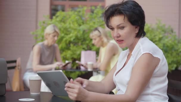 一个自信的黑发女人在户外咖啡馆里用平板电脑。成功的高加索女商人在网上冲浪的肖像。在阳光明媚的夏日，网上购物的无忧无虑的女人放松了. — 图库视频影像