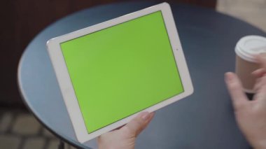 Beyaz kadın ellerinde tablet yeşil ekran yakın plan. Sosyal medya, uygulama ya da internette sörf yapan ve dışarıda kahve içen tanınmamış bir kadın. Modern yaşam tarzı.