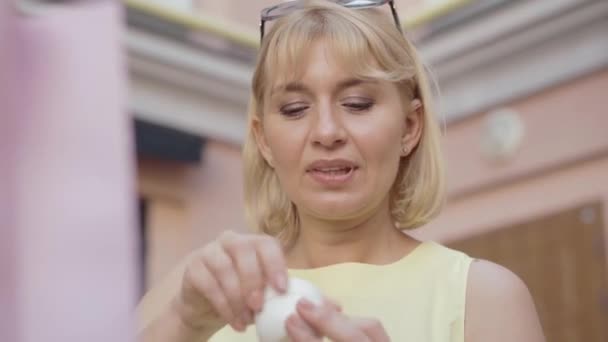 Задоволена блондинка пахне зволожувачем на вулицях міста. Портрет прекрасної середньодорослої кавказької жінки, що тримає банку з кремом для обличчя і посміхається. Органічна косметика. — стокове відео