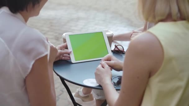 Tiro sobre o ombro de mulheres médias-adultas positivas navegando na Internet em tablet. Amigos alegres conversando e olhando para a tela verde. Senhoras modernas caucasianas usando dispositivo com cromakey ao ar livre. — Vídeo de Stock