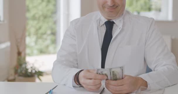 Médico feliz irreconocible contando dólares y sonriendo. Médico masculino caucásico satisfecho calculando ganancias o sobornos en el cargo. Un hombre rico que trabaja en medicina. Sede del cine 4k ProRes. — Vídeos de Stock