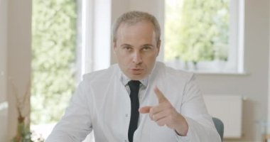 Parmağını kaldırıp kameraya konuşan katı bir doktor. Kafkasyalı doktor Covid-19 'un tehlikede olduğunu blog ya da video konferansında açıklıyor. Sinema 4k ProRes Merkezi.