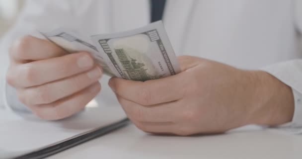 Gros plan des mains masculines caucasiennes comptant les dollars. Homme méconnaissable en uniforme de médecin tenant un paquet d'argent. Corruption en médecine. Médecin calculant le salaire. Siège social Cinema 4k ProRes. — Video