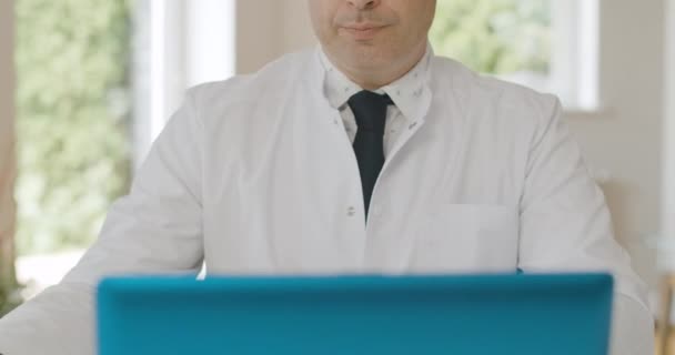 Médico masculino irreconocible sosteniendo frasco con medicamentos y apuntando a las drogas. Médico caucásico grave hablando en el ordenador portátil selfie cámara de publicidad o remedio de prescripción. Sede del cine 4k ProRes. — Vídeo de stock