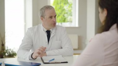 Hastanedeki hastayla ciddi bir doktor konuşuyor. Tıbbi muayeneden sonra saygıdeğer beyaz hekim kadın portresi. Klinikte müşteriyle çalışan orta yaşlı bir adam..