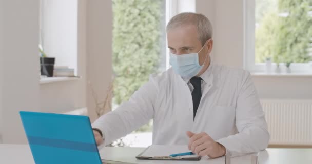 Doctor agotado cerrando laptop, quitándose la mascarilla y recostándose. Retrato del hombre caucásico cansado trabajando en línea en el bloqueo pandémico de Covid-19. Sede del cine 4k ProRes. — Vídeo de stock