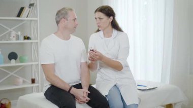 Genç, güzel, beyaz bir doktor hastane koğuşunda orta yaşlı bir adama ilaç veriyor. Erkek hastaya ilaç yazan kendine güvenen bir kadın doktorun portresi. Sağlık hizmetleri.